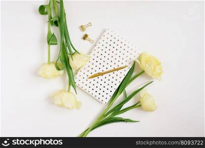 A bouquet of spring yellow tulips, a notebook on a white background and a golden pen. The concept of spring, women’s and mother’s day, birthday or blogging