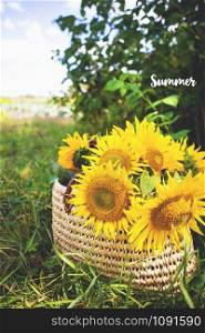 A bouquet of sunflowers lies in a straw bag on the green grass. The inscription summer.. A bouquet of sunflowers lies in straw bag on the green grass. The inscription summer.