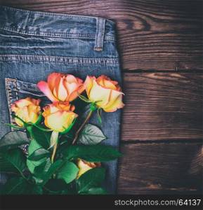 A bouquet of yellow flowering roses on blue jeans, empty space on the right