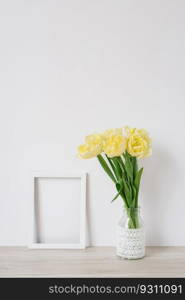 A bouquet of yellow flowers and an empty white frame for photos on a light background with copy space, space for free text. Framing workshop. Bright holiday certificate. Spring memories. Postcard.