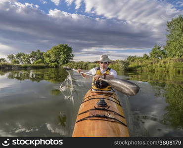 a bow view of a senior male paddling a home-built wooden sea kayak on a lake in Colorado