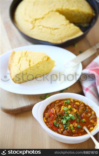 A bowl of chili with wedge of cornbread and butter