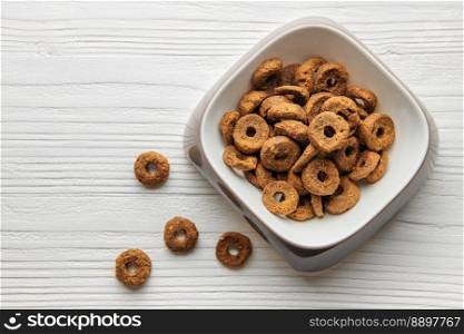 A bowl of dog food on a wooden floor. Granules of dry fodder in the form of rings.