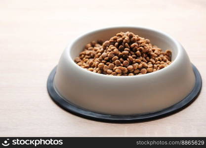 A bowl of dog food on a wooden floor. Dry food in granules.