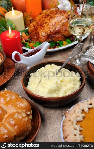 A bowl of mashed potatoes on a table among the pumpkin pie, baked turkey, cranberry-orange sauce, a glass of white wine for Thanksgiving