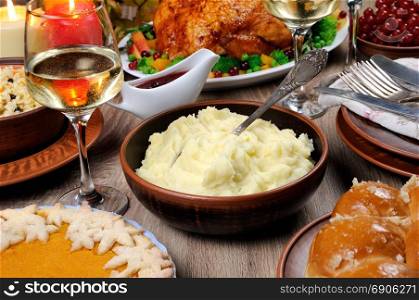 A bowl of mashed potatoes on a table among the pumpkin pie, baked turkey, cranberry-orange sauce, a glass of white wine for Thanksgiving