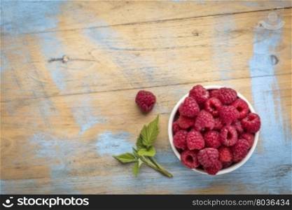 a bowl of red raspberries fresh from a garden on wood with a copy space
