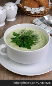 A bowl of soup with dill sauce and parsley on the table with croutons