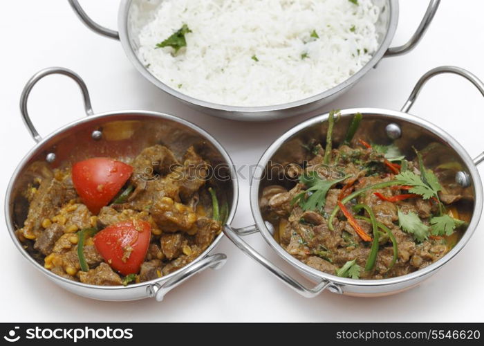 A bowl of spiced lamb curry with coriander leaves and slivers of red and green chillies, next to a bowl of Lahore-style lamb curry with split peas and some rice.