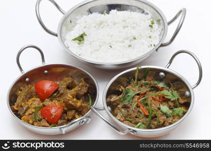 A bowl of spiced lamb curry with coriander leaves and slivers of red and green chillies, next to a bowl of Lahore-style lamb curry with split peas and some rice.