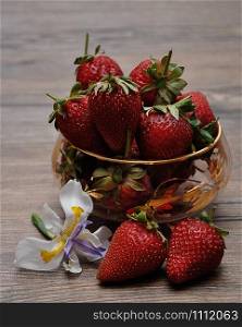 A bowl of strawberries displayed with an African Iris on a wooden background