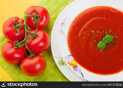 A bowl of tomato soup on a green place mat with tomatos on the vine