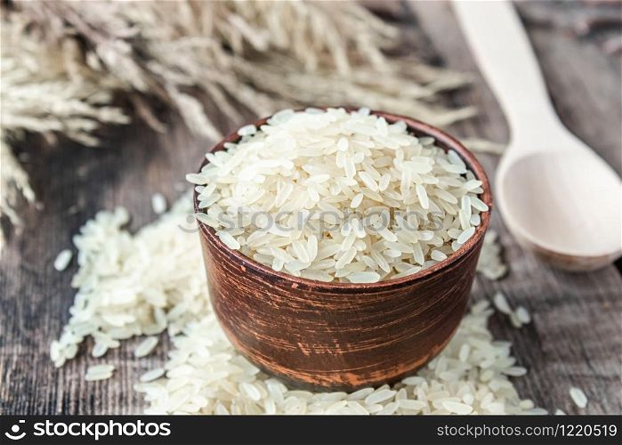 A bowl of white rice next to a pile of rice on a background of old boards. Jasmine rice for cooking. Close-up.. A bowl of white rice next to a pile of rice on a background of old boards. Jasmine rice for cooking.