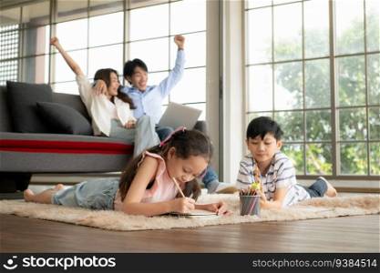 A boy and a daughter from an asian family. The children are having fun in the art of drawing. Mom and Dad enjoyed playing games on the laptop.