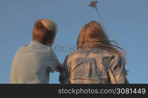 A boy and a girl launch a kite in a strong wind. In the background a kite flies in the sky. Sunset.