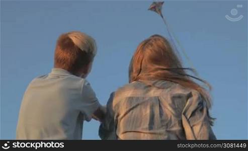A boy and a girl launch a kite in a strong wind. In the background a kite flies in the sky. Sunset.