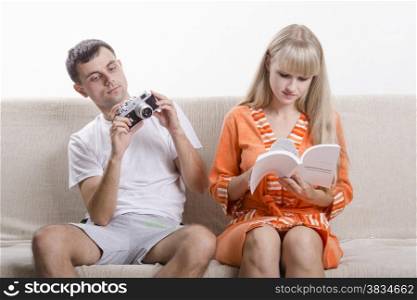 A boy and a girl sitting on the couch. The guy turns to the camera in your hands, the girl reads instruction