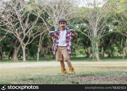 A boy childs holding climbing stick and rehearsal on the lawn wearing hiking shose is over size.Child having fun in summer.