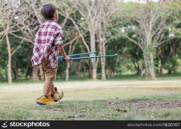 A boy childs holding climbing stick and rehearsal on the lawn wearing hiking shose is over size.Child having fun in summer.