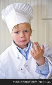 A boy, dressed in a chef&rsquo;s uniform, showing his dirty fingers, sticky with the sweet ingredients he&rsquo;s been tasting. Selective focus on the boys face