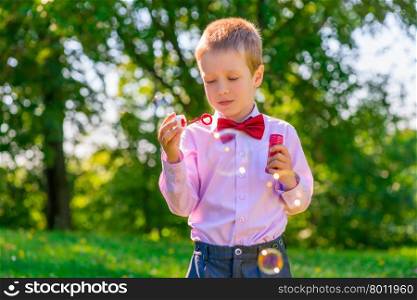 a boy in a green park blowing soap bubbles