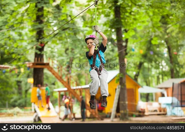 A boy in a helmet and safety equipment in adventure ropes park on the background of nature. Child in a adventure playground