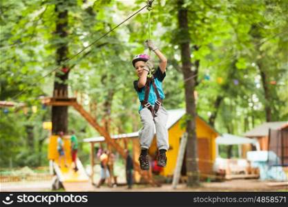 A boy in a helmet and safety equipment in adventure ropes park on the background of nature. Child in a adventure playground