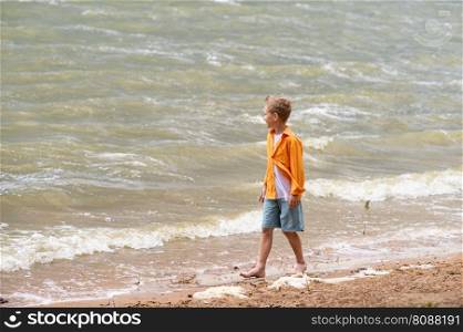 A boy in an orange shirt on the seashore.. A boy in an orange shirt on the seashore