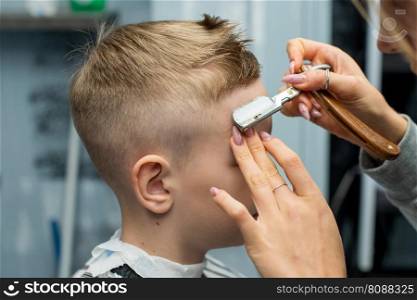 A boy is sitting in a barbershop, doing his hair with a sharp razor for a haircut. A boy is sitting in a barbershop, doing his hair with a razor for a haircut