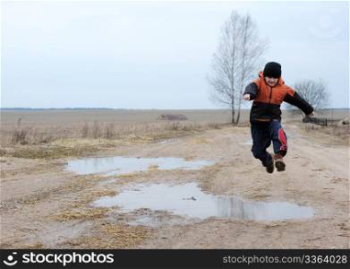 A boy jumps over a puddle on a rural road
