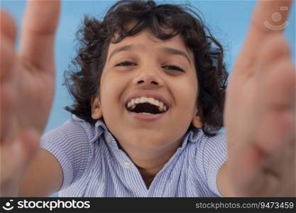 A BOY LAUGHING WHILE RAISING HANDS AND LOOKING AT CAMERA