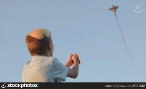 A boy launch a kite in a strong wind. In the background a kite flies in the sky. Sunset.
