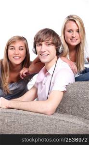 a boy listening music and two blonde girls behind a couch