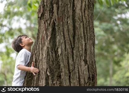A boy stands hugging a big tree and looking up on tree.Pollution issue.
