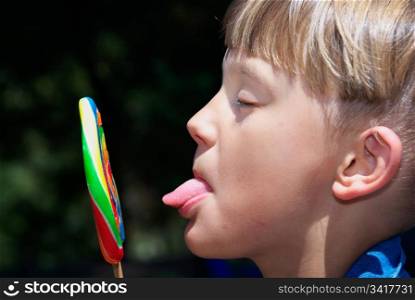 a boy sticks his tongue out to lick the lollipop. boy licking a lollipop