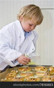 A boy, wearing a cook&rsquo;s jacket, spreading sprinklers over sweet bread