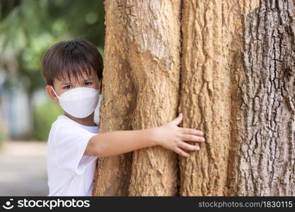 A boy wearing a mask stands hugging a big tree and looking at camera.Pollution issue.