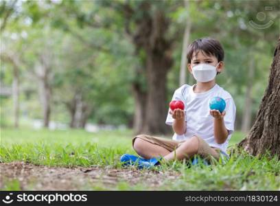 A boy wearing a mask to prevent pollution holding a globe and heart in hand looking at camera .Love health love earth concept