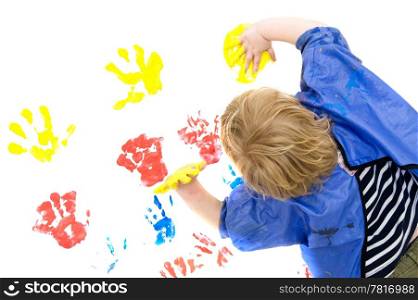 A boy wearing an apron busy finger painting, with his hands covered in yellow paint