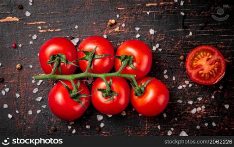 A branch of fresh tomatoes with pieces of salt. Against a dark background. High quality photo. A branch of fresh tomatoes with pieces of salt.