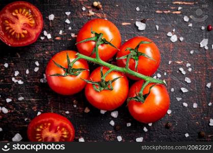 A branch of fresh tomatoes with pieces of salt. Against a dark background. High quality photo. A branch of fresh tomatoes with pieces of salt.