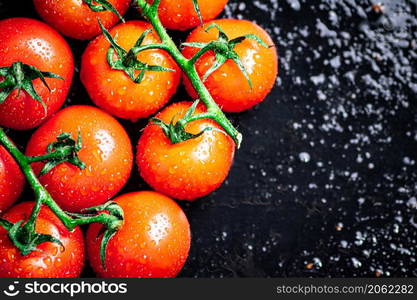 A branch of ripe tomatoes on a wet table. On a black background. High quality photo. A branch of ripe tomatoes on a wet table.