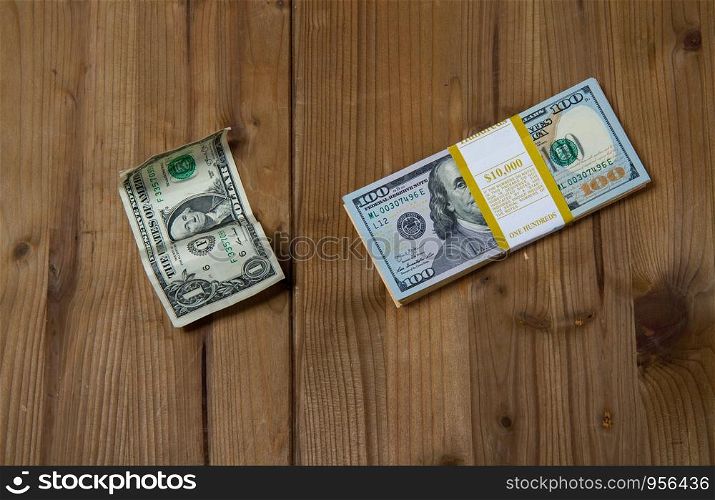 a brand new bundle of hundred-dollar bills and a crumpled one-dollar banknote on a wooden surface. one and thousands