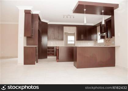 A brand new designer kitchen of dark brown wood in a new house with a tiled floor and white ceiling.