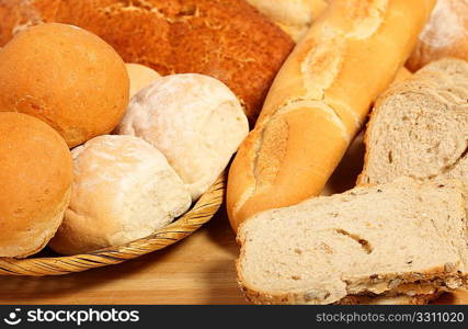 A breadbasket with rolls on a breadboard with sliced and unsliced loaves.