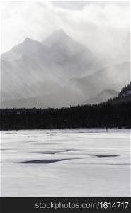 A break in the deep snow winds its way toward at atmospheric scene of the Canadian Rockies in Kananaskis Country.