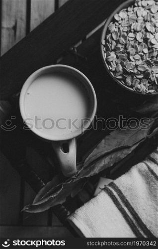 A breakfast of a cup of oat milk with oat seeds over a wooden plank in black and white