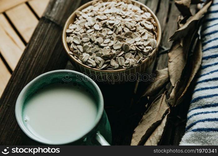 A breakfast of a cup of oat milk with oat seeds over a wooden plank