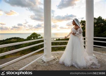 A bride in a wedding dress in a gazebo with columns on the seashore looks towards the sea a. A bride in a wedding dress in a gazebo with columns on the seashore looks towards the sea