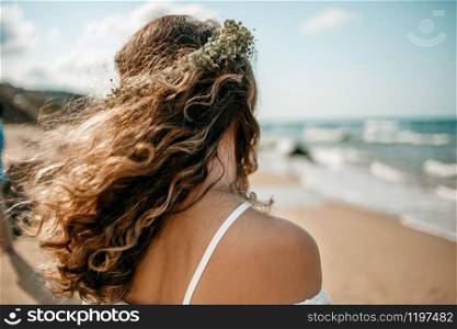 a bride in a white wedding dress on the beach with a wreath of flowers on her head. view from the back